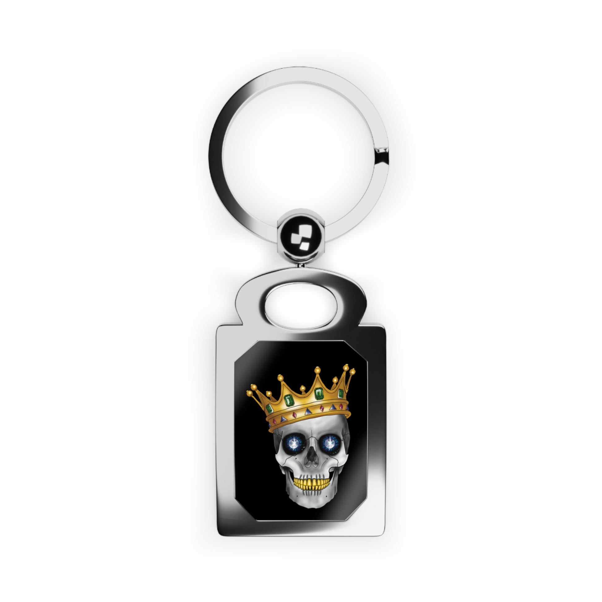 Rectangular silver keychain with a bold design framed inside: a skull with gleaming gold teeth, glittering sapphire eyes, and a lavish gold crown—all set against a dramatic black background, serving royal attitude with a side of macabre flair.