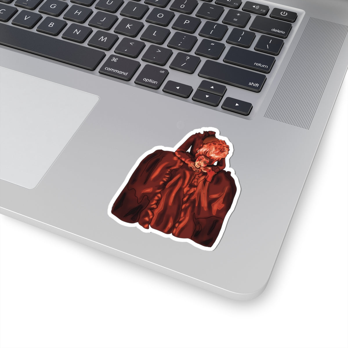 Small sticker on a computer featuring a drawing of Marie Antoinette dressed in red, holding her own head after beheading.
