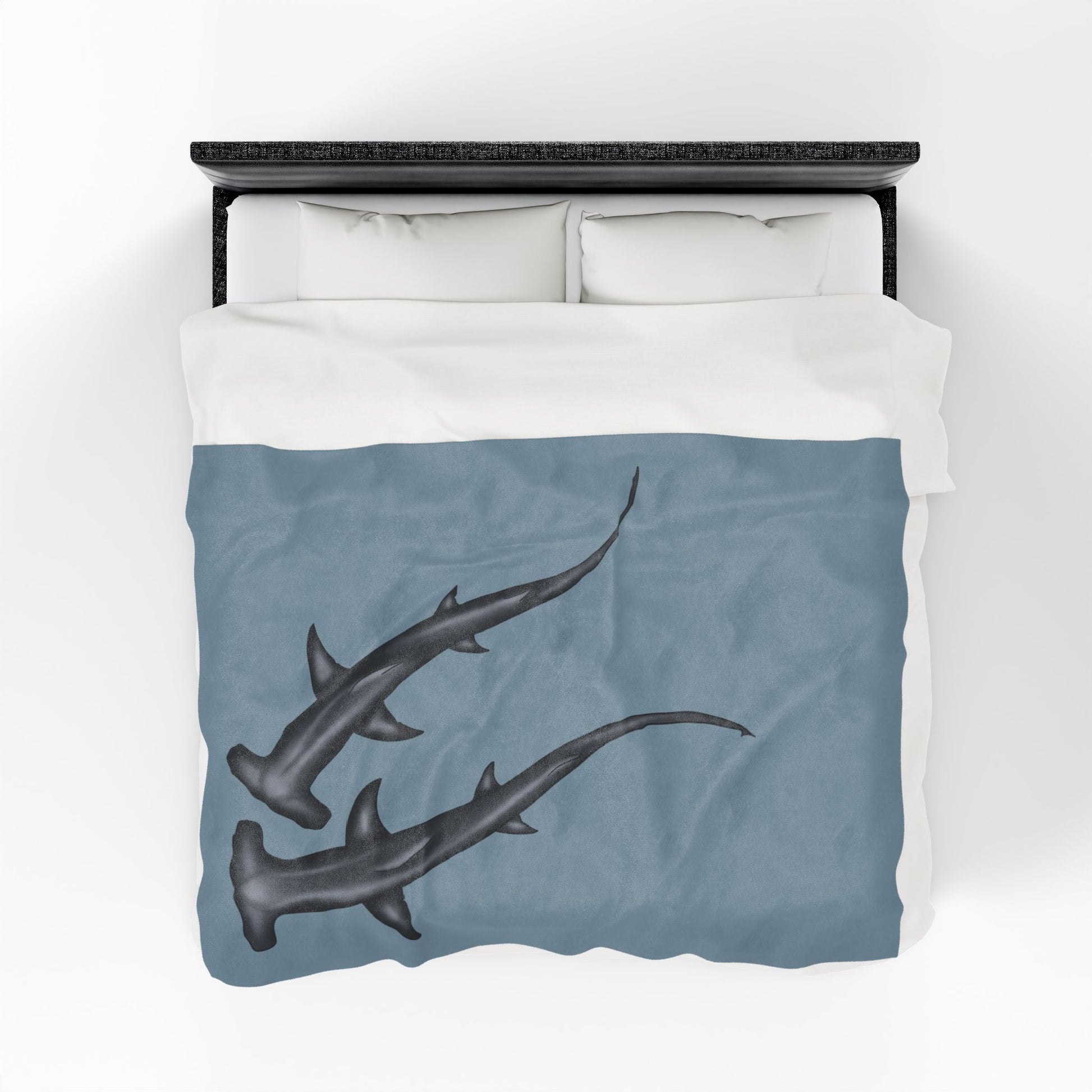 A large blue-grey velveteen plush blanket featuring two hammerhead sharks gliding through the fabric like it's their personal ocean—perfect for wrapping yourself in comfort with a side of bite. Shown on a queen size bed from above.