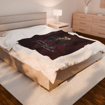 A medium burgundy velveteen plush blanket featuring a smirking Edgar Allan Poe, a brooding raven, and crimson roses—perfect for cozying up with your favorite haunting thoughts and the poetic quote, "All that we see or seem is but a dream within a dream. Shown on a queen size bed.