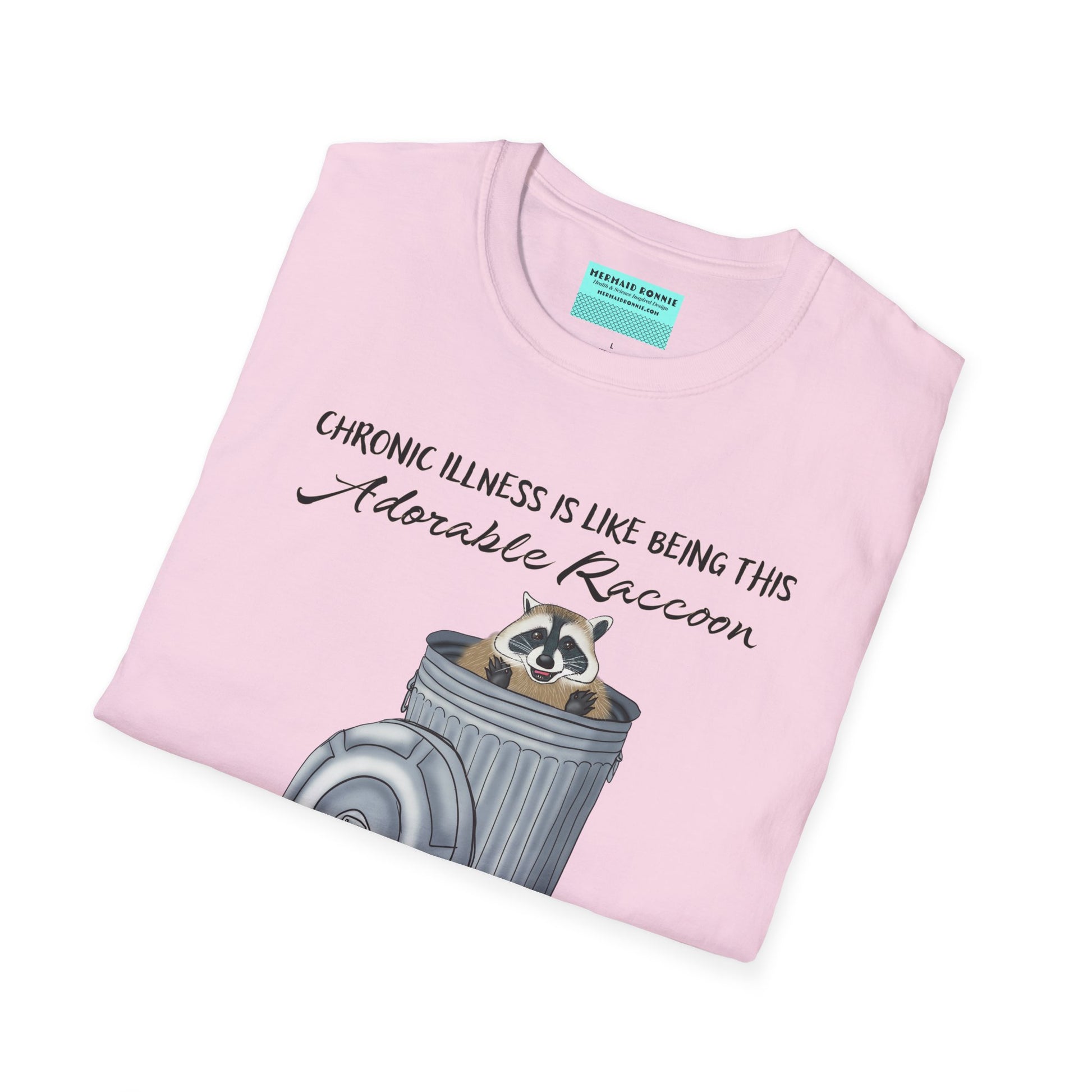Folded light pink t-shirt featuring an illustration of a raccoon in a metal trash can, with the phrase 'Chronic illness is like being this adorable raccoon living in a trash can body' printed on it.